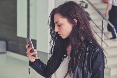 Ofis binasının arka planında akıllı telefonu olan bir kız.