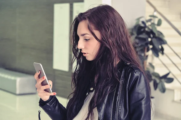 Модный портрет красивой женщины со смартфоном на фоне интерьера офисного здания — стоковое фото