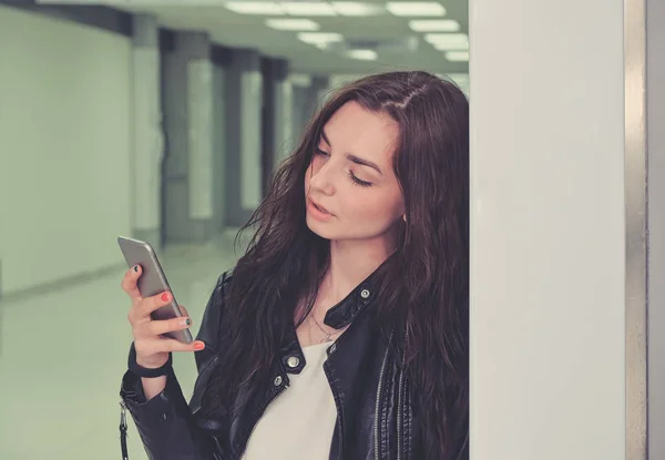 Portret van mooi meisje met behulp van haar smartphone leunend achterover de muur — Stockfoto