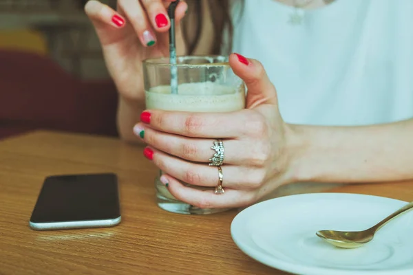 Γυαλί με καφέ στο χέρι ενός κοριτσιού με Smartphone που βρίσκεται στο τραπέζι — Φωτογραφία Αρχείου