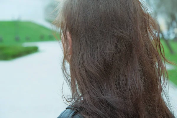 Femme mignonne aux cheveux longs regardant la rue tout en se promenant dans la ville. Vue arrière d'une femelle méconnaissable portant un leaser noir debout à l'extérieur le jour du printemps . — Photo