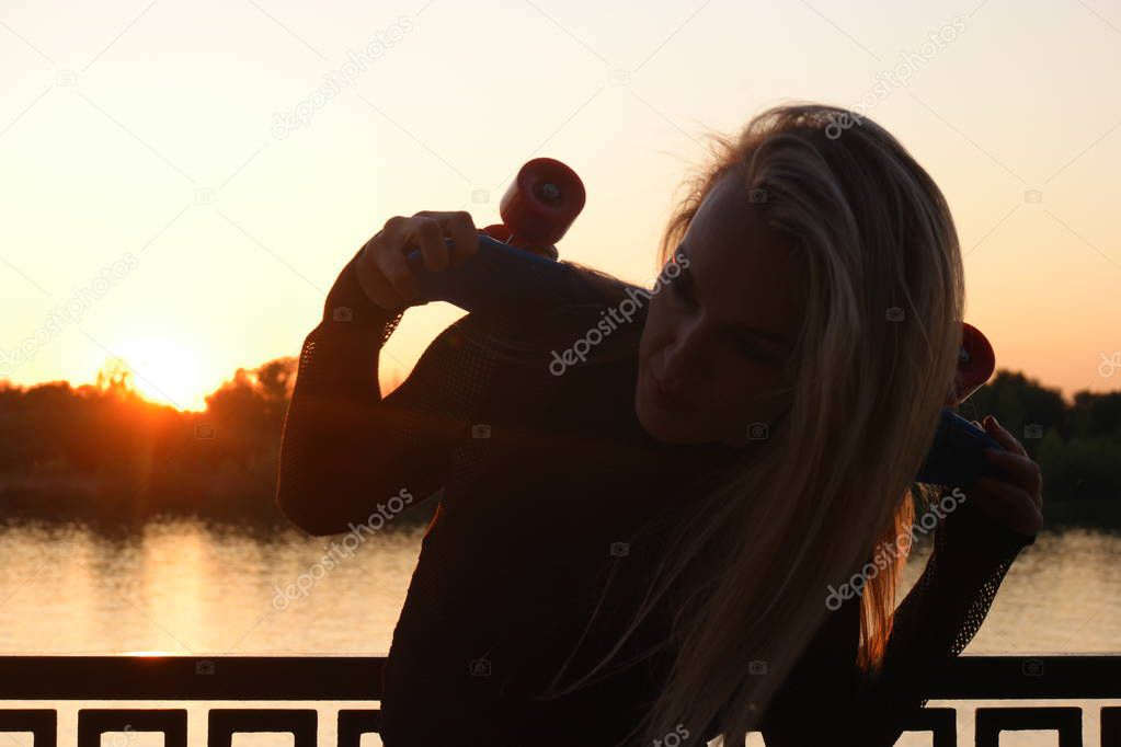 Blond hair scateboarder posing bended in front of sunset on waterfront