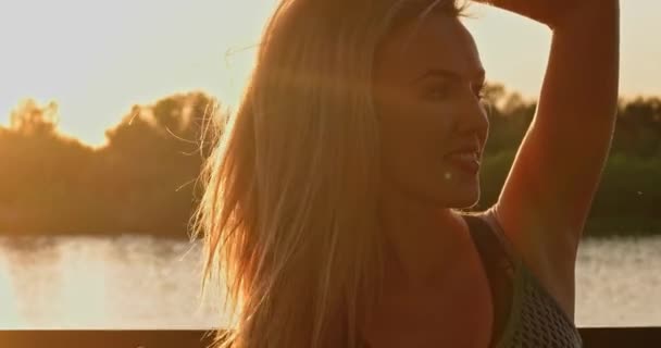 Hermosa mujer rubia en el paseo marítimo en la puesta del sol — Vídeos de Stock