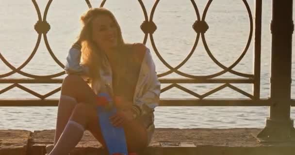 Jeune femme dans la trentaine avec une drôle de petite planche à roulettes assise sur le front de mer — Video