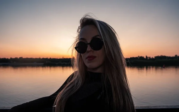 Doordachte vrouw in haar 30s poseren in de voorkant van het meer zonsondergang in zonnebril — Stockfoto