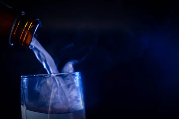 La garganta de las botellas colgaba sobre el vidrio. De la botella sale un chorro de vapor y licor, simbolizando el espíritu maligno del alcohol . — Foto de Stock