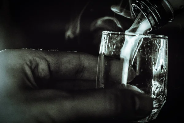 Una mano sostiene un vaso sobre el que cuelga el cuello de las botellas y sale un chorro de vapor, tentando al espíritu maligno del alcohol. . —  Fotos de Stock