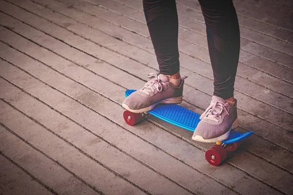 Het meisje staat op een klein blauw skateboard, haar benen dragen legging en sportschoenen. — Stockfoto
