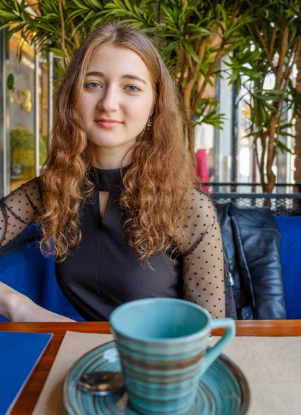 Młoda kobieta siedzi za szczeblem w kawiarni i przed nią znajduje się mały elegancki kubek z wzorem kółek o różnych kolorach. — Zdjęcie stockowe