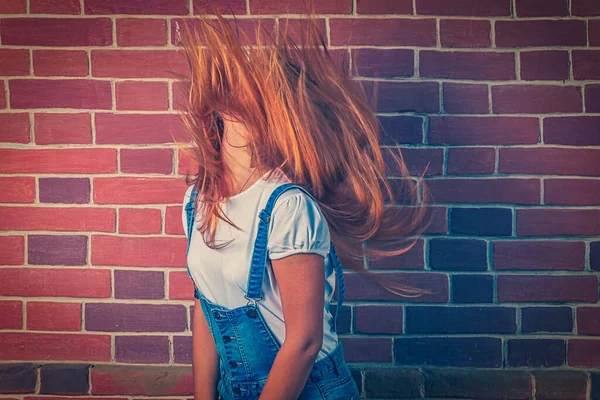 Profil der blonden jungen Dame, die ihr Haar über Backsteinhintergrund schüttelt. — Stockfoto