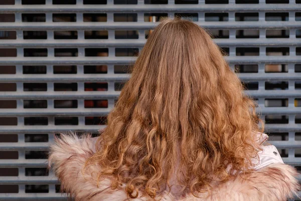 View from the back of a woman with curly red hair. She is posing in front of metal grid — Stock Photo, Image