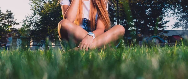 Menina adolescente está sentada de pernas cruzadas na grama vermes vista do olho — Fotografia de Stock