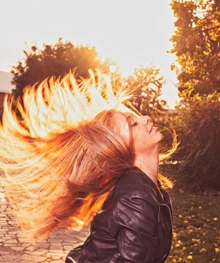 Sarışın bir kadın gün batımında elini sıkar, arka ışıklandırmalı çekim yapar. Güneş ışığıyla dolu saçlarıyla egzotik bir şekilde dans ediyor