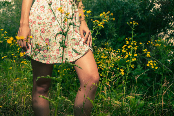 A young girl wears a light summer dress and stands in tall grass so we can see the knees of her gentle bare feet.
