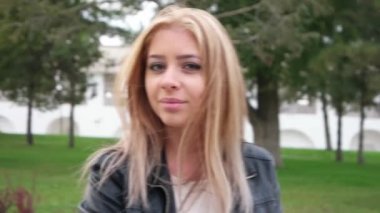 Uzun saçlı sarışın sokakta poz veriyor, kameraya bakıyor, vesikalık fotoğraf çekiyor.