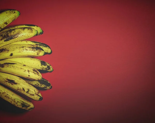 赤の背景に有機バナナのレトロなスタイルのイメージトップビュー バナナの束は熟成過程を示す暗斑とオレンジの背景に横たわっている — ストック写真