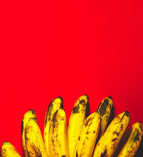 コピースペースの上の眺めがある赤い背景の多くのバナナ バナナの束は熟成過程を示す暗斑とオレンジの背景に横たわっている — ストック写真