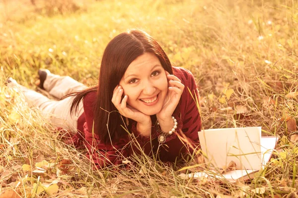 Gelukkig vrouw liggend met boek in de herfst gras — Stockfoto