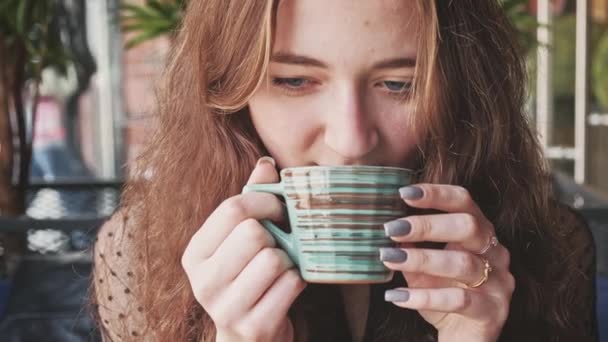 Ung flicka med rött hår får en mycket varm kopp te och sedan sätter den tillbaka på ett tefat. — Stockvideo