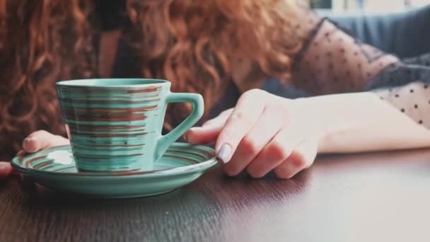 En kvinde snurrer eftertænksomt en keramisk kop kaffe på en tallerken og dens belyst i ryggen. – Stock-video
