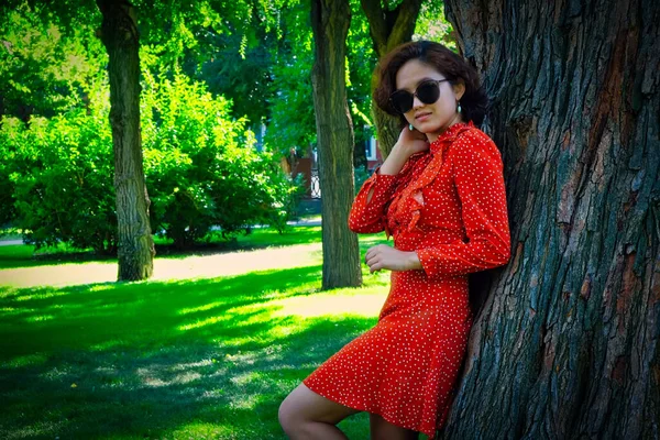 Glückliches Mädchen im roten Kleid lehnt Park Baum im Sommer — Stockfoto