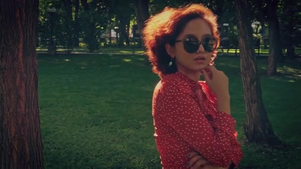 Mooi aziatisch meisje met korte ronding haar poses in het park gekleed in een retro jurk en zonnebril — Stockvideo