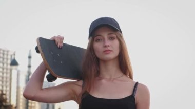 Omzunda kaykayıyla poz veren güzel ve şık bir genç kadın.