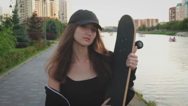 Mujer joven hermosa y de moda posando con un monopatín en el terraplén — Vídeo de stock