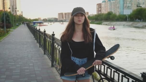 Una giovane ragazza gira il suo skateboard sulla riva del fiume — Video Stock