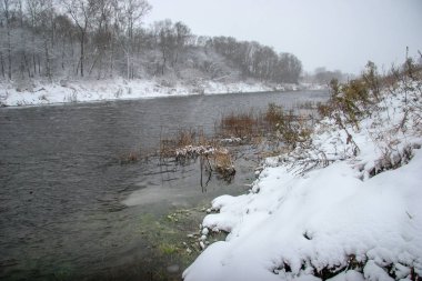 Kışın nehir manzarası. Karla kaplı kıyıları olan bir nehir. Memele Nehri 'nde kar yağacak. Letonya 'da kış. Kar, kış boyunca ormanı ve zenginliği kaplamıştı..