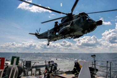 Helikopter kurtarma görevi denizde zor fırtınalı havalarda. NATO askeri helikopter ve gemi Baltık Denizi, Letonya; NATO askeri helikopter ve gemi Baltık denizde eğitim.