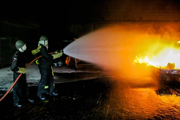 Firefighters training for fire fighting in Germany. Firefighter in fire protection suit spraying water to fire with smoke. Firefighter fighting fire attack, during training exercise