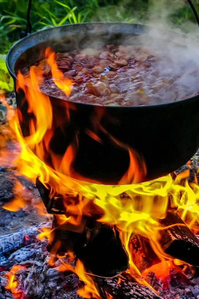 Cooking soup in cast iron boiler on burning campfire. Pot with soup over the open fire outdoors. Tourism in Latvia. Cooking soup in a pot on campfire.
