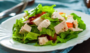 tavuk ve soğan, marul, domates masada beyaz tabak içinde taze sebze salatası