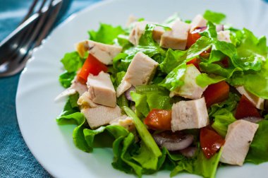 tavuk ve soğan, marul, domates masada beyaz tabak içinde taze sebze salatası