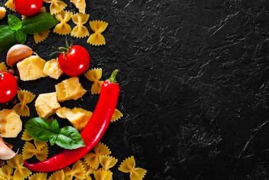 Gıda arka plan. İtalyan pasta - yemek pişirmek için malzemeler farfalle makarna, kırmızı biber, kiraz domates, fesleğen, karabiber, sarımsak, parmesan peyniri ile kopya alanı koyu arka plan üzerinde. üstten görünüm