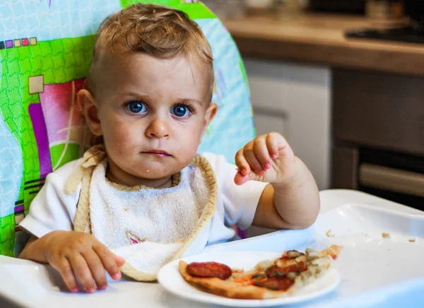 椅子と皿にピザのスライス上に小さな男の子が座っています 不健康な食べ物 — ストック写真