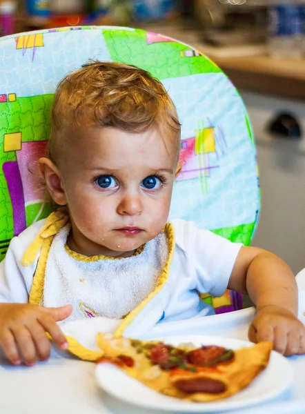椅子と皿にピザのスライス上に小さな男の子が座っています 不健康な食べ物 — ストック写真