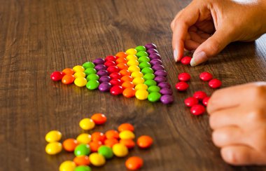 kadın eli bile renkli şekerler sırasının bir ahşap arka plan üzerinde toplar.