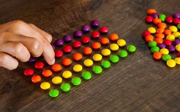 Woman Hand Collects Even Row Colorful Candies Wooden Background — Stock Photo, Image