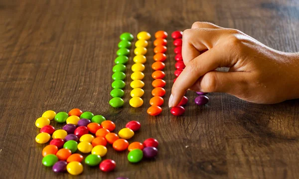 Kadın Eli Bile Renkli Şekerler Sırasının Bir Ahşap Arka Plan — Stok fotoğraf