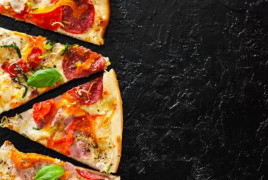 dilim Pizza ile Mozzarella peyniri, jambon, domates, salam, biber, biber baharat ve taze fesleğen. İtalyan pizza.on siyah arka plan. kopya alanı ile. üstten görünüm