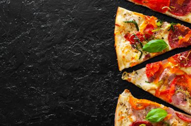 dilim Pizza ile Mozzarella peyniri, jambon, domates, salam, biber, biber baharat ve taze fesleğen. İtalyan pizza.on siyah arka plan. kopya alanı ile. üstten görünüm