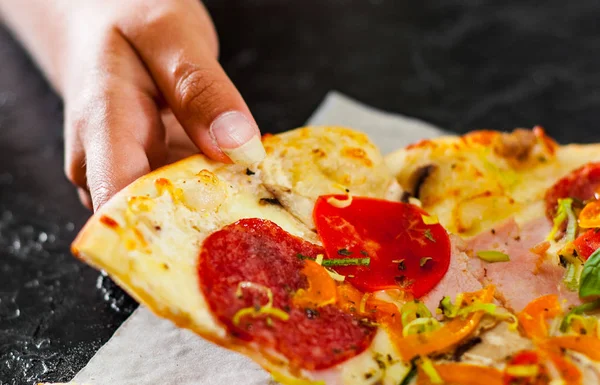 woman Hand takes a piece of Pizza with Mozzarella cheese, Ham, Tomatoes, salami, pepper, pepperoni, Spices and Fresh Basil.