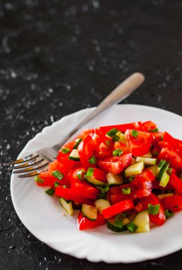 siyah arka plan üzerine beyaz tabakta domates, salatalık ve yeşil soğan ile taze sebze salatası.