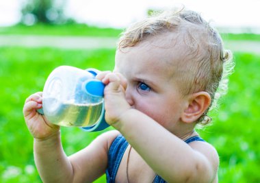bir parkta çim üzerinde oturan ve şişeden içme küçük bebeğim.