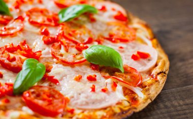 Pizza Mozzarella peyniri, jambon, domates, biber, baharat ve taze fesleğen. Ahşap arka plan üzerinde İtalyan pizza.