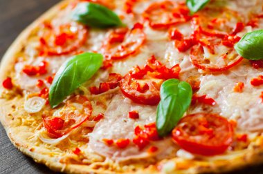 Pizza Mozzarella peyniri, jambon, domates, biber, baharat ve taze fesleğen. Ahşap arka plan üzerinde İtalyan pizza.