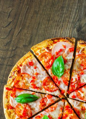 Pizza Mozzarella peyniri, jambon, domates, dilimlenmiş biber, baharatlar ve taze fesleğen. Ahşap arka plan üzerinde İtalyan pizza.