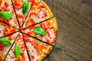 Pizza Mozzarella peyniri, jambon, domates, dilimlenmiş biber, baharatlar ve taze fesleğen. Ahşap arka plan üzerinde İtalyan pizza.